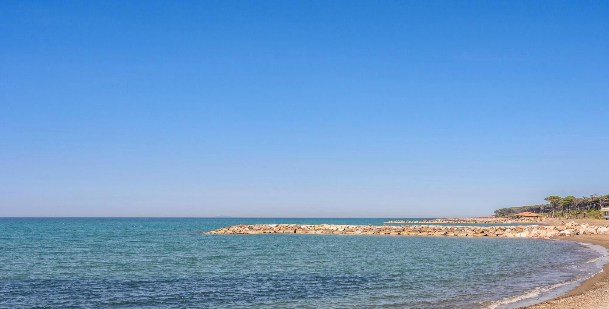 A coastal beach with clear skies, calm waters, and rocky formations.