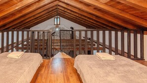 Ein gemütliches Schlafzimmer im Dachgeschoss mit Holzbalken, einer Treppe und zwei Betten mit gefalteter Bettwäsche.