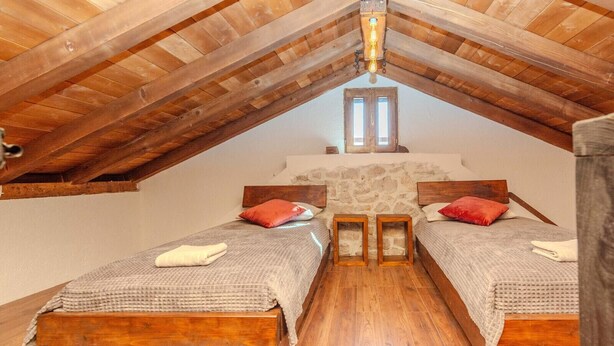 Un dormitorio con dos camas de madera, paredes de piedra y techo inclinado con vigas de madera.
