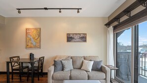 Un salon comprenant un canapé, une table basse et une table à manger avec des chaises. Une grande fenêtre offre une vue sur l’extérieur.