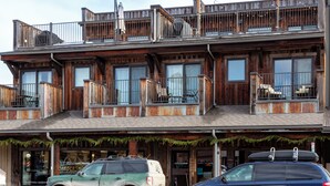 Un immeuble de deux étages, avec un salon de coiffure au rez-de-chaussée et un restaurant au deuxième étage. Deux voitures sont garées devant.