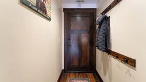 Un couloir avec une porte en bois, un porte-manteau sur lequel est accroché un veston, et un tapis orné d’un motif de buffle.