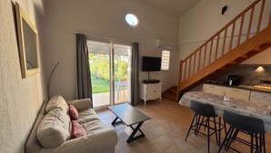 Ein Wohnzimmer mit einer Couch, einem kleinen Tisch, einem Fernseher und einer Treppe, die zur Küche führt.