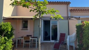 Ein überdachter Patio-Bereich mit Tisch und Stühlen, einem roten Liegestuhl und einem kleinen Baum.