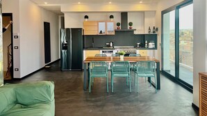 Een moderne keuken met een centraal eiland, roestvrijstalen apparatuur en een eethoek met groene stoelen.