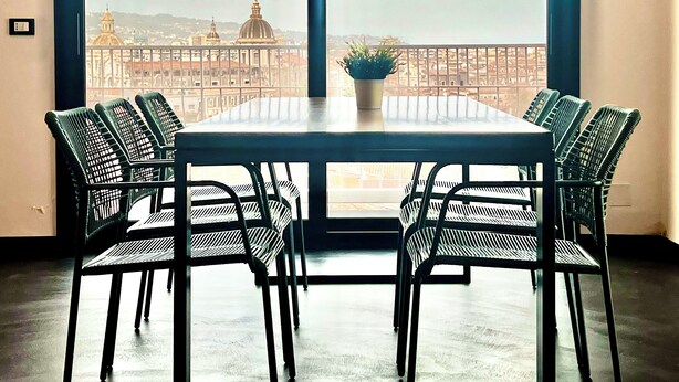 Een balkon met een tafel, stoelen, een bloempot en uitzicht op een stadsgezicht met koepelgebouwen.