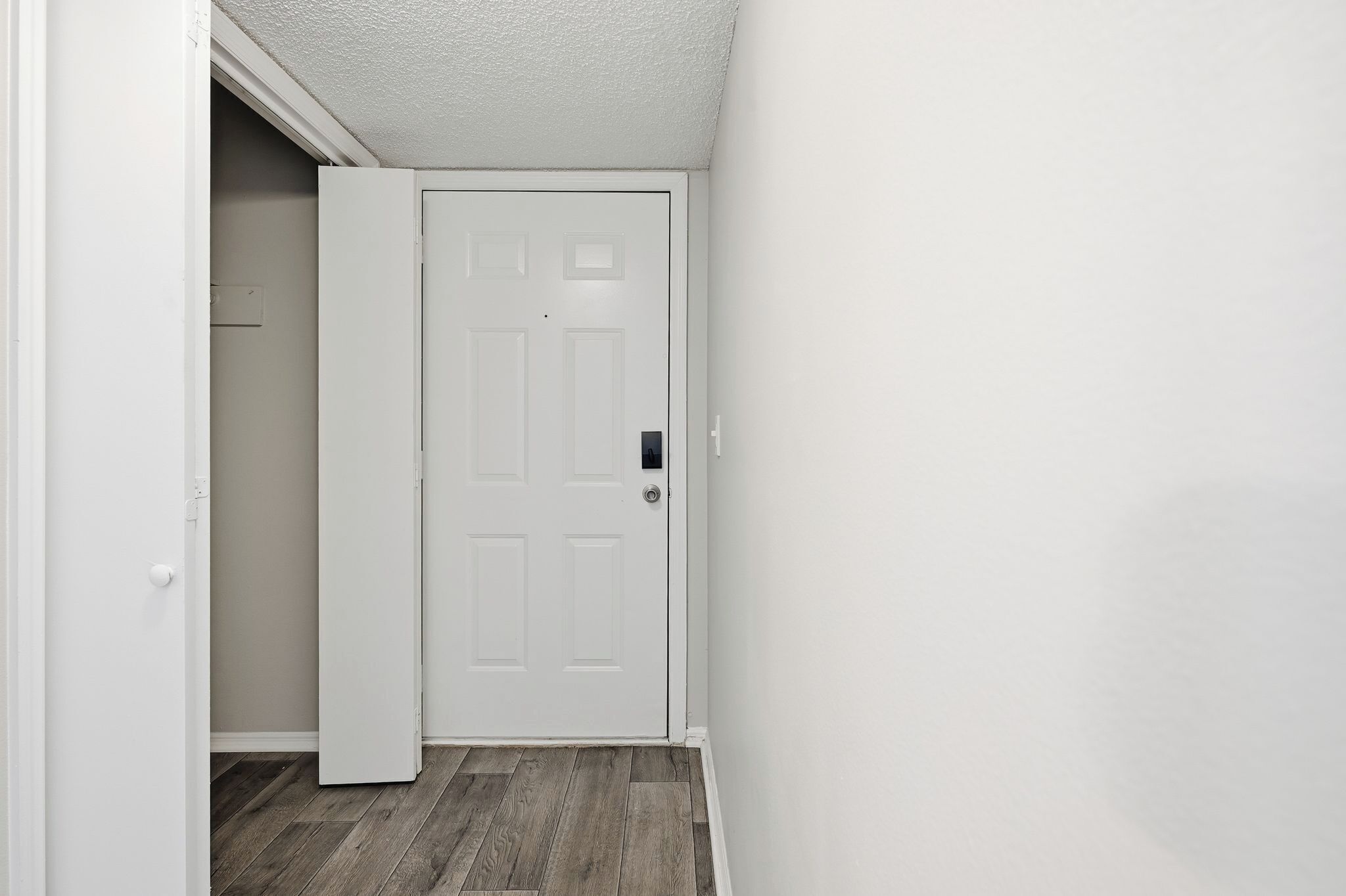 A hallway with a white door, wooden flooring, and white walls.