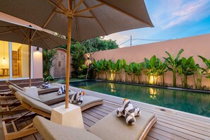 A poolside area with lounge chairs, an umbrella, and a wooden deck. - Villa Terracotta (Tabanan)