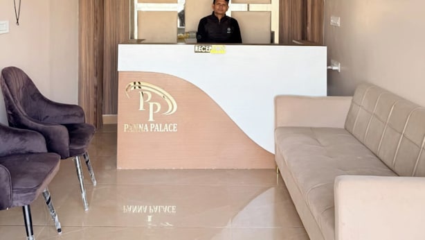 A reception area with a modern design, featuring a reception desk, a ceiling fan, a flat-screen TV, and a seating area with two sofas and two chairs. - Panna Palace (Mathura)