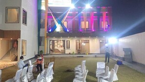 An outdoor seating area with rows of chairs covered in white fabric, a building with illuminated signage, and a staircase leading to an entrance. - Panna Palace (Mathura)