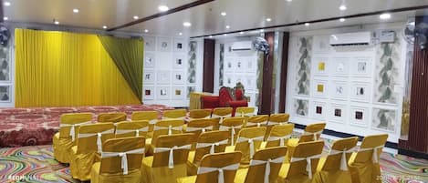 A conference room with rows of yellow chairs, a red sofa, and a stage with a microphone.