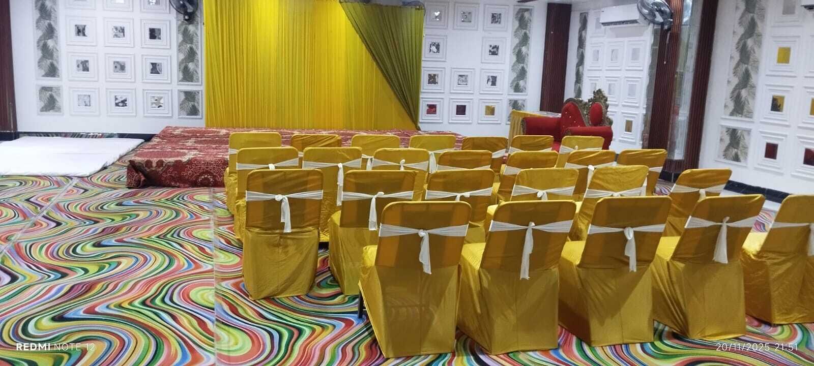 A room with rows of yellow chairs with white sashes, a red sofa, and a stage with a yellow backdrop.