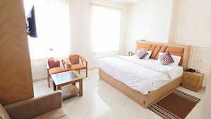 A hotel room with a bed, a sofa, a table, and a ceiling fan. - Panna Palace (Mathura)