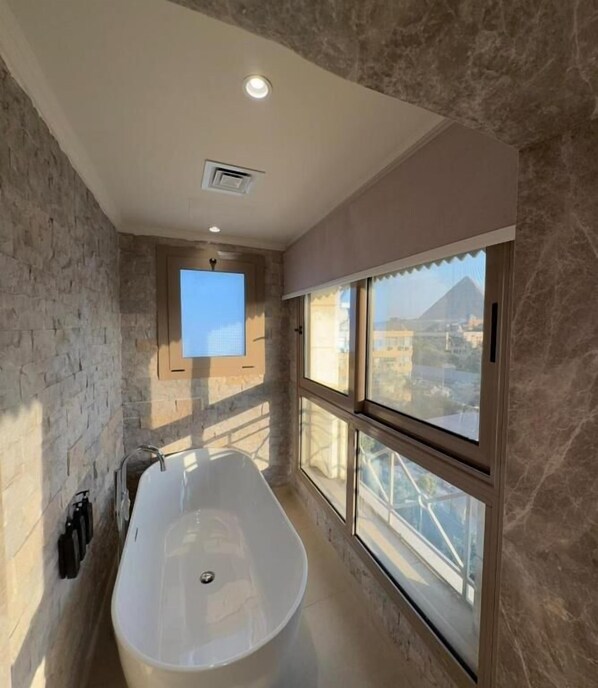 Une salle de bain moderne avec une baignoire sur pieds, de grandes fenêtres et un mur en pierre.