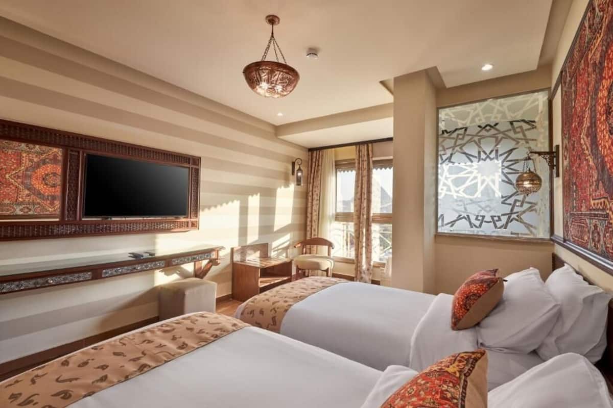 A hotel room with two beds, a desk, a chair, a television, and a decorative wall.
