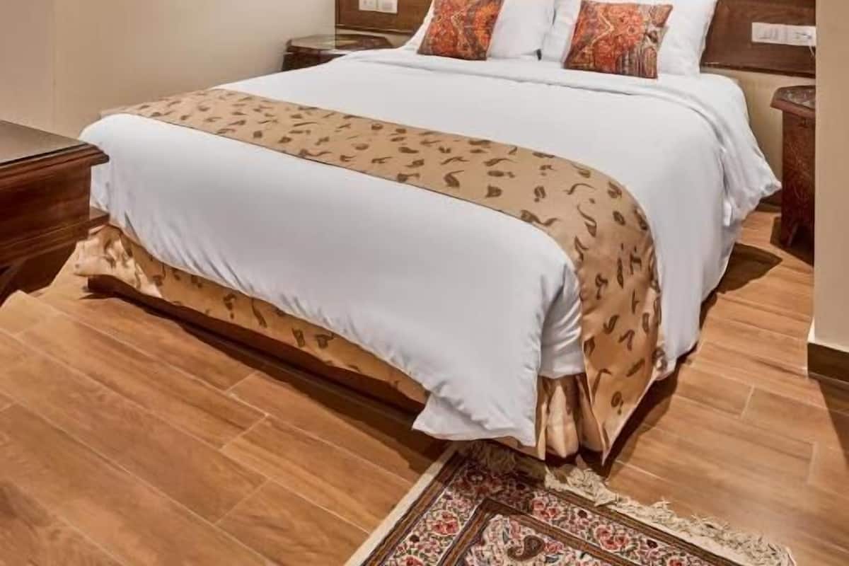 A hotel room with a large bed, a patterned rug, a wall tapestry, and a ceiling light fixture.