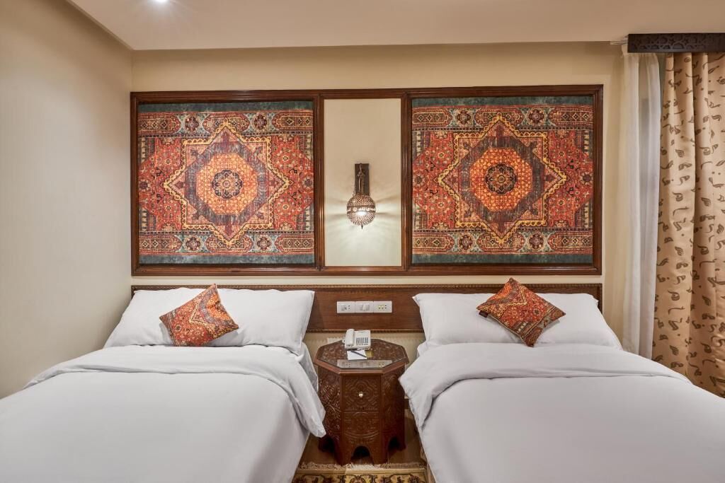 A hotel room with two beds, a nightstand, a decorative wall hanging, and a hanging light fixture.