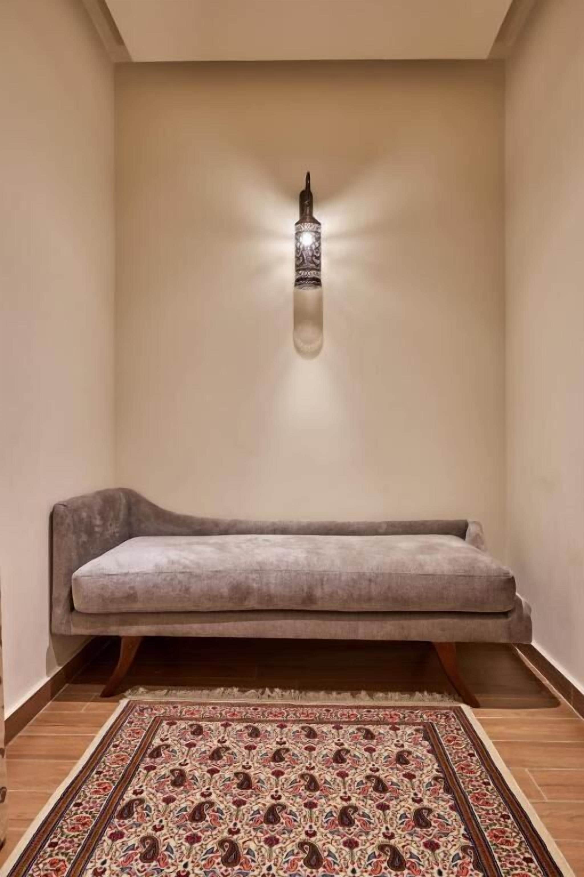 A cozy room with a cushioned bench, a patterned rug, and a wall-mounted light fixture.