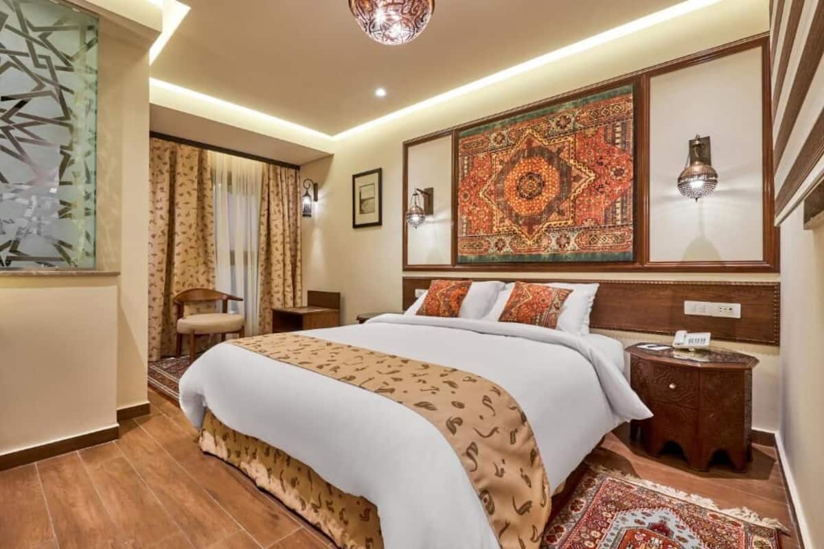 A hotel room with a large bed, a nightstand, a wall-mounted lamp, and a decorative rug.