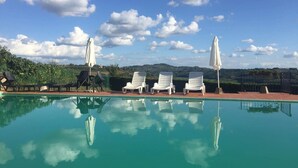 A clear swimming pool with lounge chairs and umbrellas, surrounded by greenery and hills. - Panorama – Apartment with Terrace and Views of the Tuscan Countryside (Montespertoli)