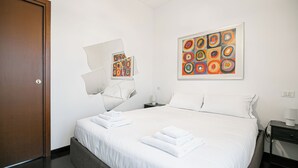 A hotel room with a large bed, white linens, a nightstand with a lamp, and two paintings on the wall. - Italianway Easy - Zuretti 57 (Milan)