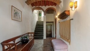 A hallway with a wooden bench, a staircase, and a wall-mounted light fixture. - Cipressina – Spacious Tuscan Apartment with Pool for Families and Groups (Montespertoli)