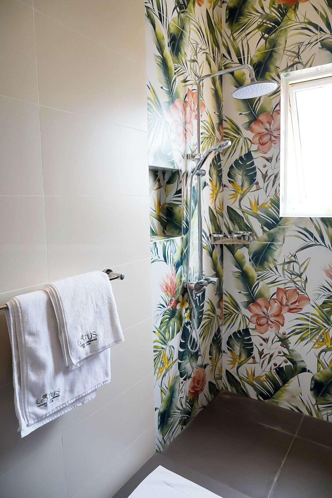 Um banheiro com cortina de chuveiro estampada com folhas e flores tropicais, uma toalha branca pendurada em um porta-toalhas e uma janela que oferece iluminação natural.