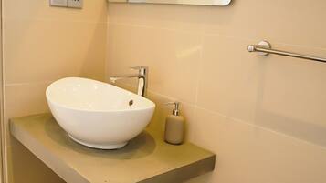 A modern bathroom with a white vessel sink, a wooden shelf, a mirror, and a towel rack.