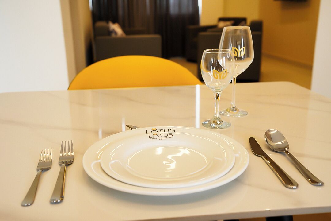 A dining table with a white plate labeled "LUTIS LOTUS," a wine glass, and cutlery.