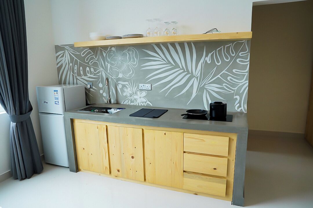 A compact kitchen with a grey countertop, wooden cabinets, and a wall with a tropical leaf pattern.