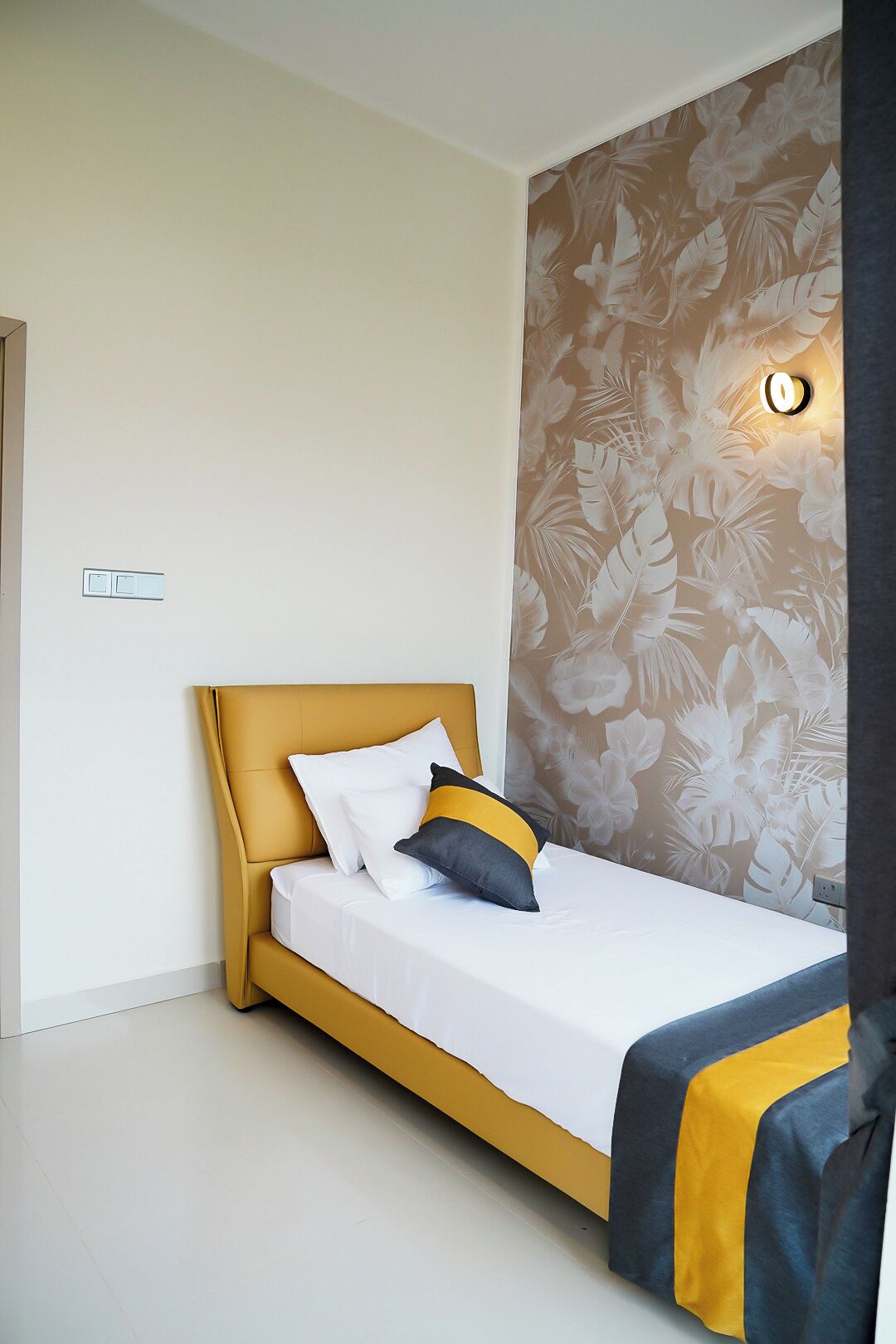 A bed with a yellow headboard, white bedding, and a floral-patterned wall.