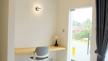 A modern hotel room with a bed, a desk with a chair, an air conditioning unit, and a view of greenery outside.