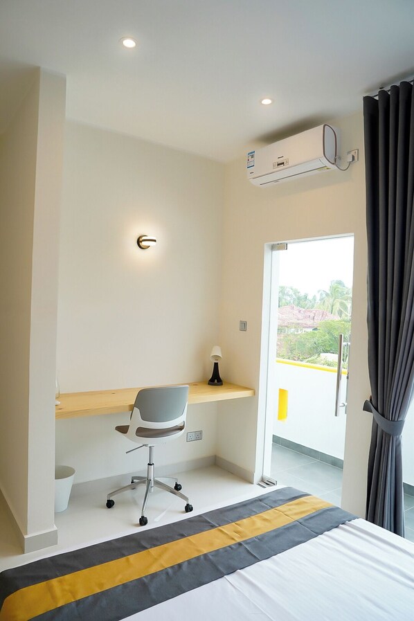 Une chambre d’hôtel moderne équipée d’un lit, d’un bureau avec une chaise, d’un système de climatisation et offrant une vue sur la verdure environnante.