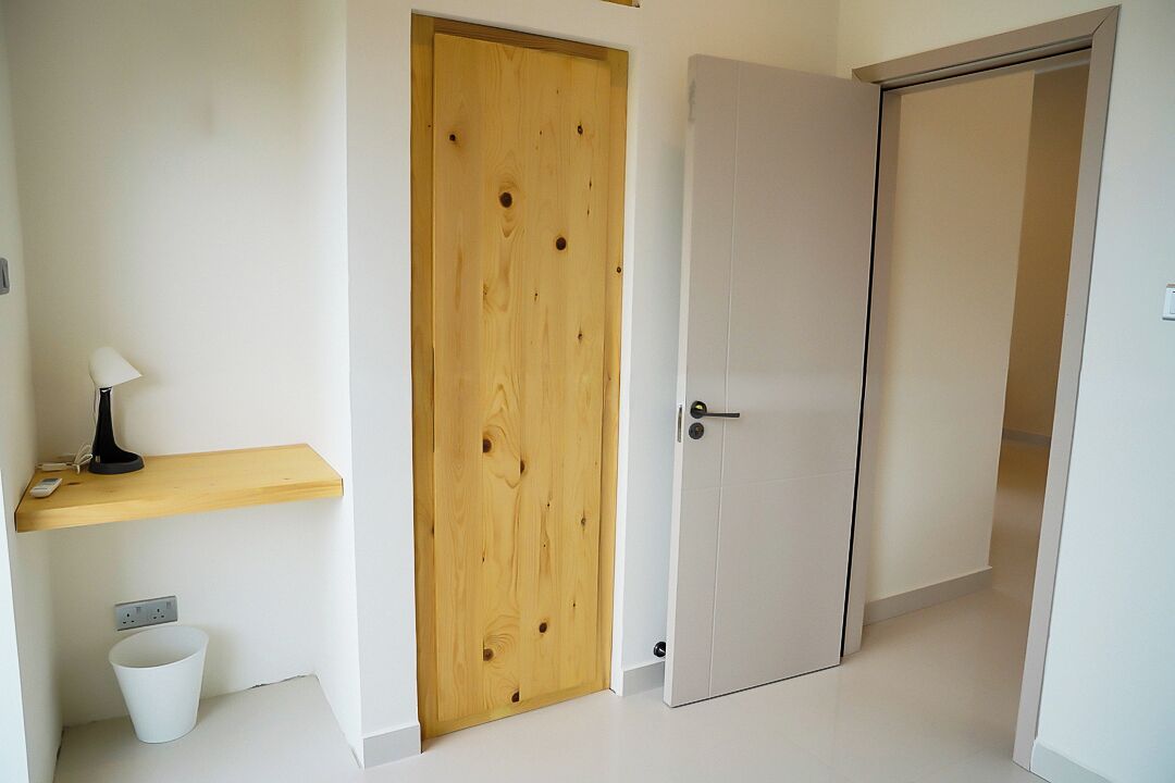 Ein Flur mit einer Holztür, einer weißen Tür, einem kleinen Regal mit einer Lampe und einer weißen Mülltonne.