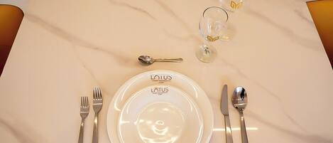 A table set with a white plate, cutlery, and two glasses on a marble table.
