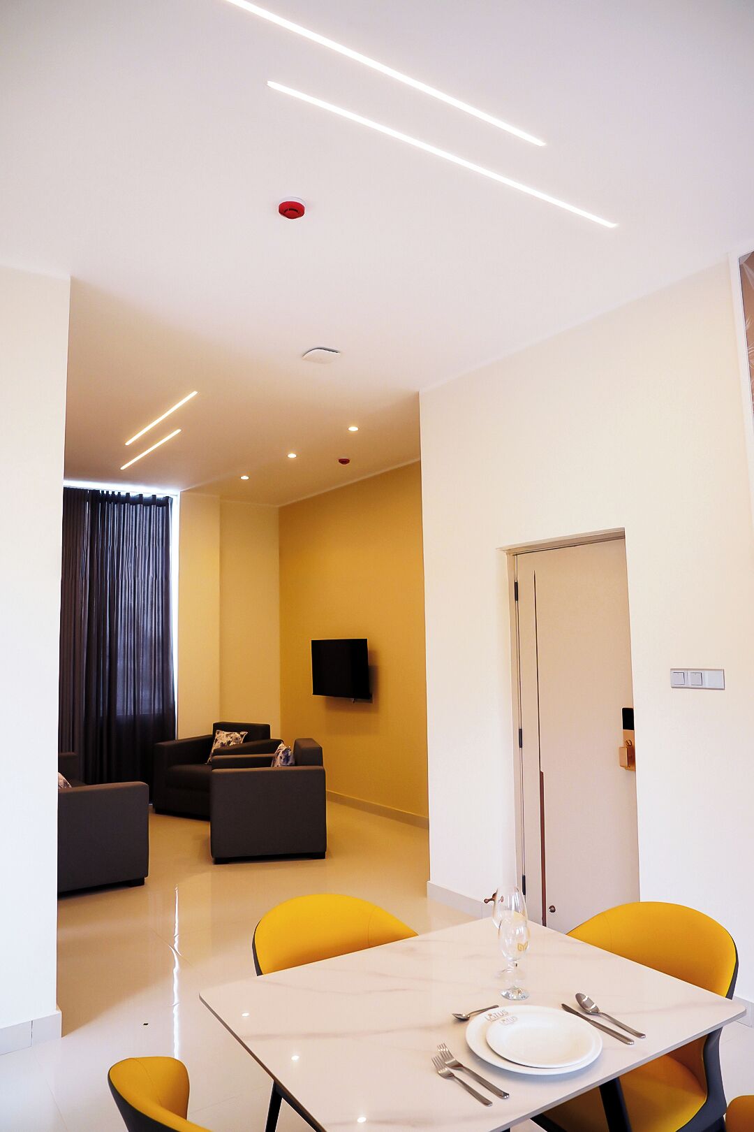 A modern living room with a sofa, a flat-screen TV, and a dining area with a table set for two.