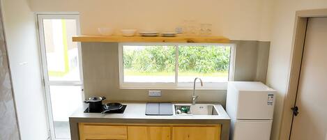 A small kitchen with a window, a sink, a stove, and a refrigerator.