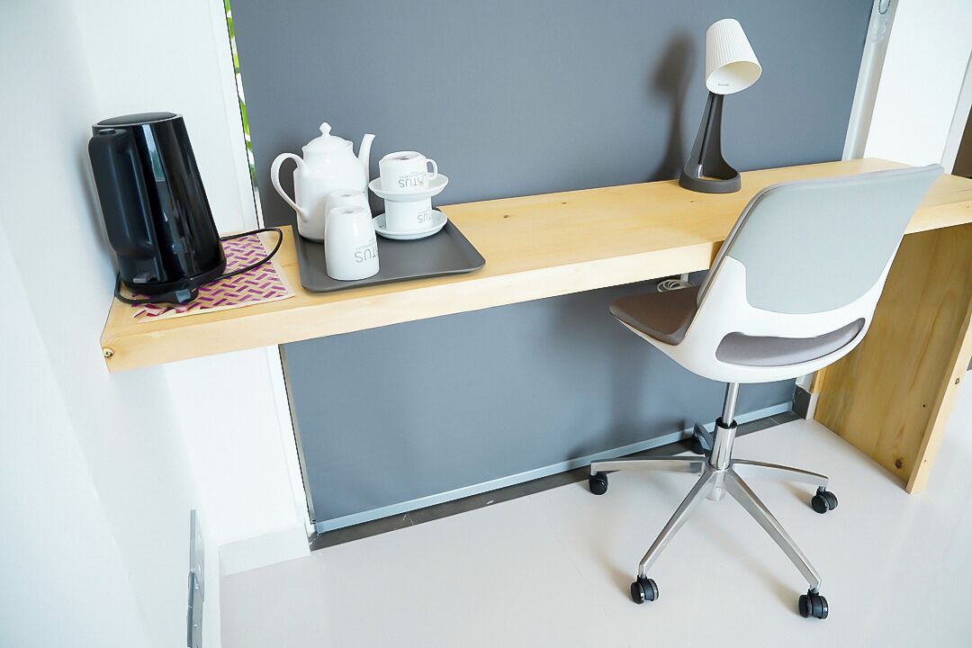 En modern arbetsplats med ett skrivbord i trä, en vit kontorsstol, en svart kaffebryggare, en vit tekanna och en vit lampa.