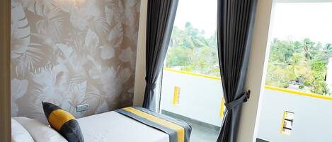A bedroom with a bed, curtains, a wall-mounted light, and a window with a view of greenery.