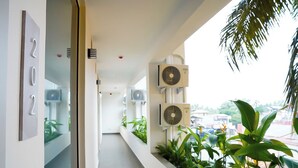 Un couloir avec un panneau indiquant les numéros des pièces, des unités de climatisation et des plantes en pot.