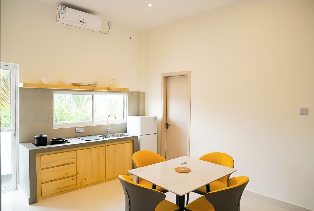 A compact kitchen with a window, a refrigerator, and a dining area with yellow chairs.