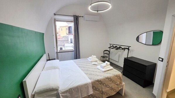 A hotel room with a bed, a dresser, a mirror, and a window with a view of buildings.