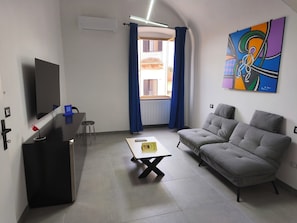A modern living room with a grey sofa, a small table, a TV mounted on the wall, and a colorful abstract painting. - Agli Archi Eco House: Sustainable and fragrance-free house in central Chieti (Chieti)