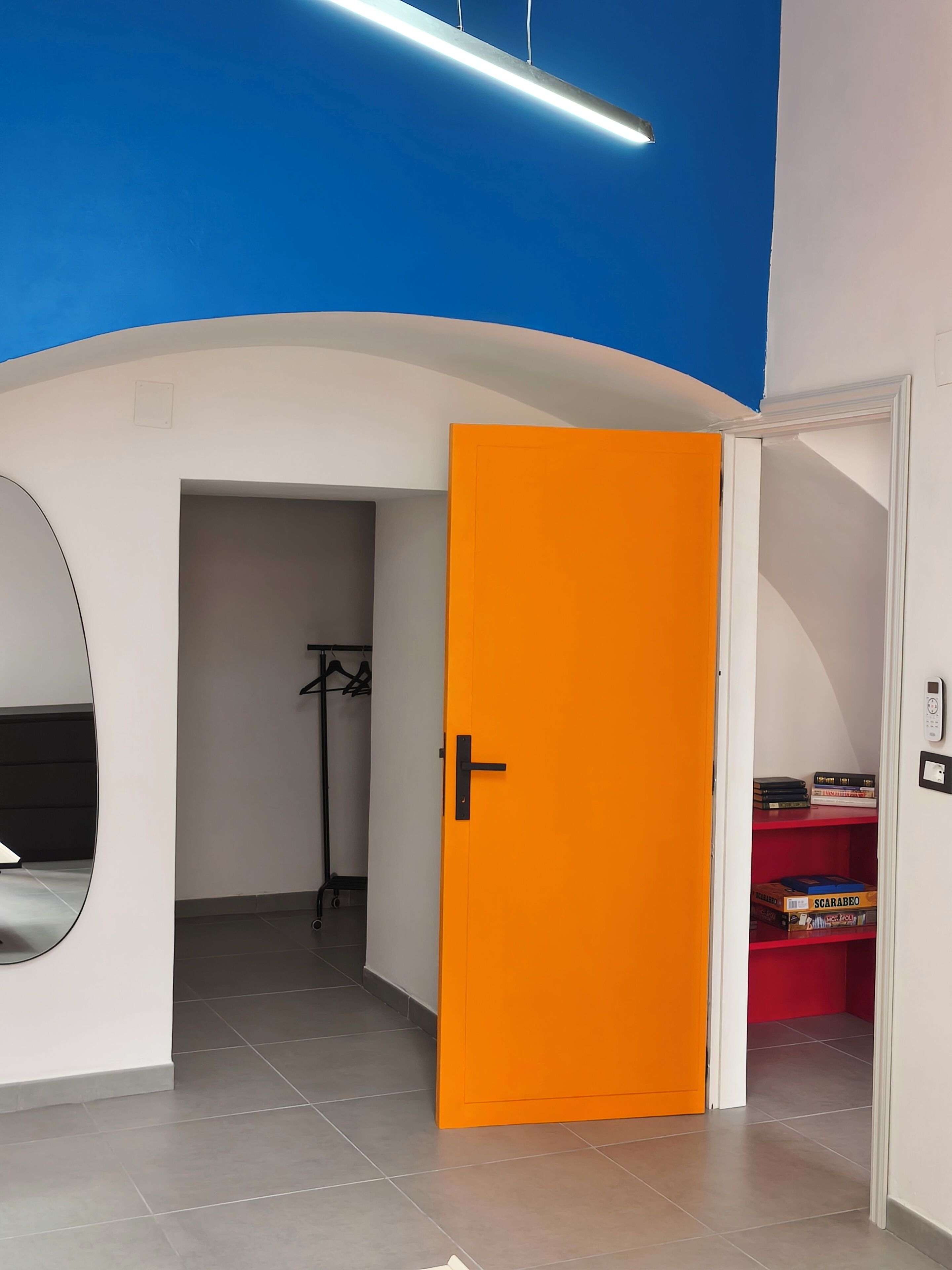 Ein Zimmer mit weißer und blauer Decke, einer orangefarbenen Tür und einem roten Regal mit Büchern.