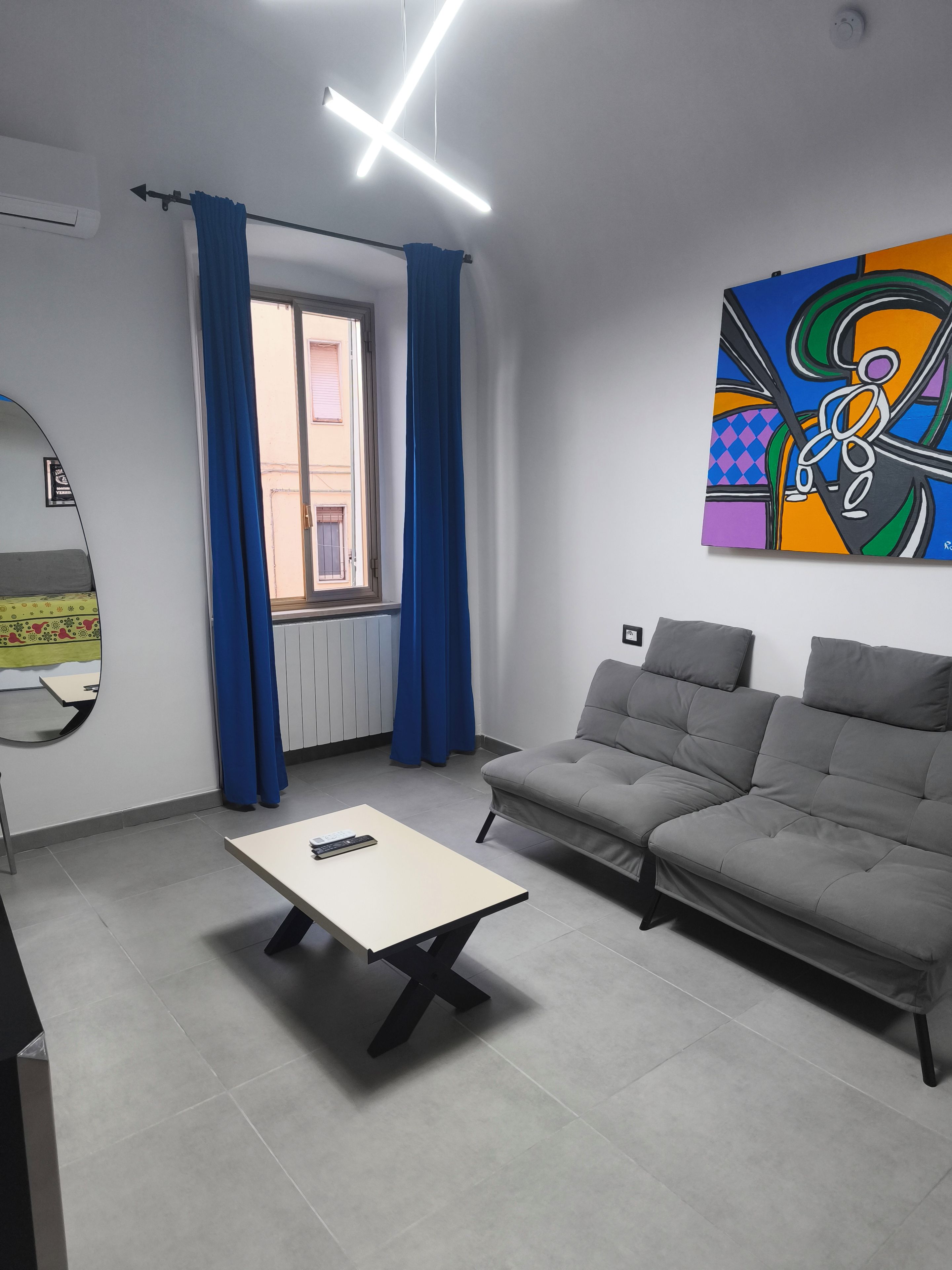 En moderne stue med en grå sofa, et lille bord og et farverigt abstrakt maleri på væggen.
