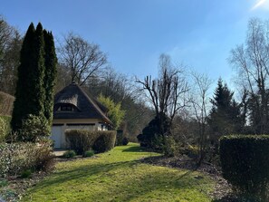 Ein Haus mit Strohdach, umgeben von gepflegten Hecken und Bäumen.