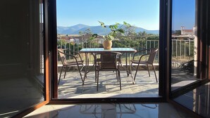 A balcony with a table and chairs, a potted plant, and a view of mountains.