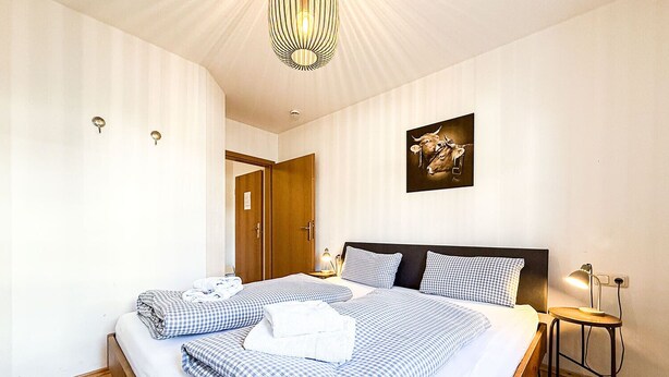 Ein Hotelzimmer mit einem großen Bett, einem Nachttisch mit Lampe, einem Wandbild und einer Tür zu einem anderen Raum.