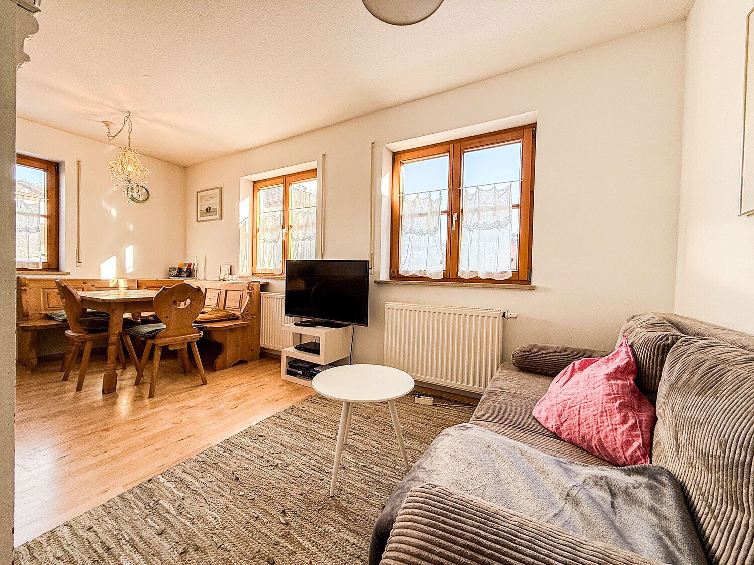 Un salon confortable avec un canapé, un téléviseur, un coin repas comprenant une table et des chaises, et de grandes fenêtres.