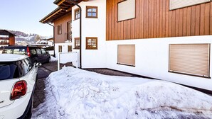 Ein Gebäude mit Holzbeschichtung und mehreren Fenstern, parkenden Autos und Schnee auf dem Boden.
